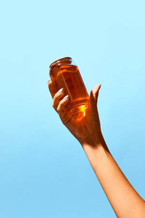 Woman holding transparent can filled with amber liquid against blue background. Minimalist mockup of beer, lemonade, soda water drinksの写真素材