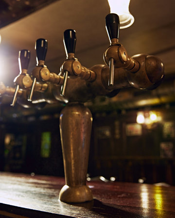 Close-up of row of shiny beer taps with handles, set against dark background with blurred bar counter. Vintage restaurant aestheticsの写真素材