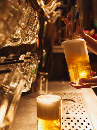 Female bartender pouring lager foamy beer from tap into glass. Luxurious vibes of bar interior