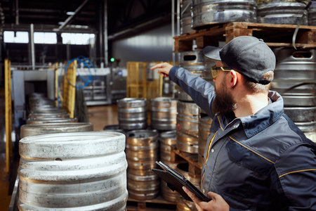 Man, brewery technologist in protective gear inspecting the production line, checking safety and...