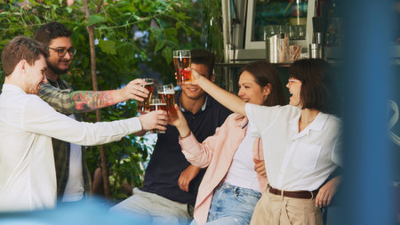 Cheers. Happy young people, men and women, friends gathering at outdoor cozy bar, drinking beer and celebrating, Lively eventの写真素材