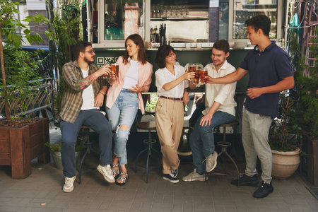 Casual hangout at outdoor bar. Young stylish men and women, friends meeting outdoor in cozy evening, drinking beer and having good conversationの写真素材