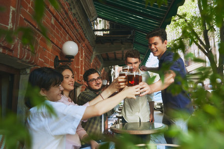 Smiling happy young people, men and women, friends gathering at outdoor bar in warm sunny evening...
