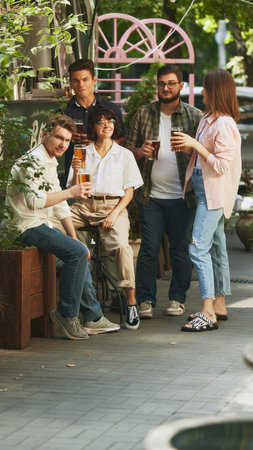 Relaxed and happy young people, men and women, friends gathering at cozy outdoor bar, pub, enjoying regressing beer. Festive atmosphereの写真素材