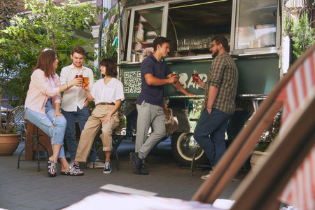 Cozy outdoor bar atmosphere where friends, group of people, men and women enjoying refreshing beer and good relaxing vibesの写真素材