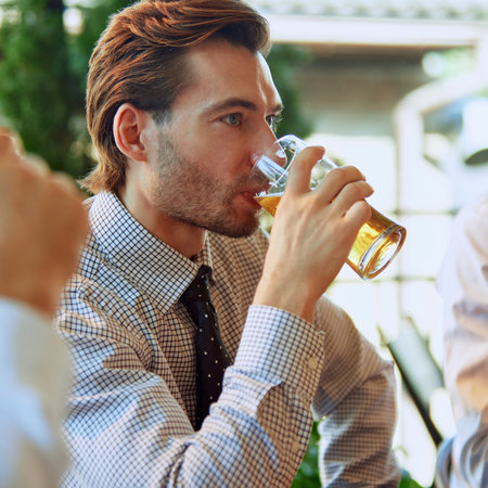 Focus on man in formal wear, sitting at outdoor bar and drinking lager beer. After work meeting with colleagues.の写真素材