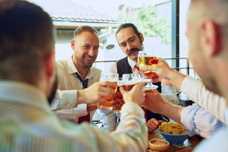Businessmen meeting at outdoor pub, drinking lager beer in joy and fun, clinking glasses in...