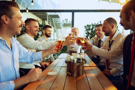 Group of smiling men, business people, colleagues sitting in pub and drinking beer, celebrating partnership, achievements and teamworkの写真素材