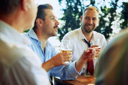 Cheerful people, businessmen, colleagues sitting at outdoor bar, restaurant, drinking beer, talking, discussing successful projects and partnershipの写真素材