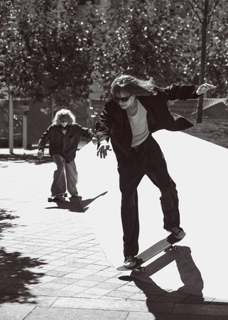 Black and white photography. Dynamic image of two young guys in stylish clothes skateboarding outdoors. Urban lifestyle, energy and style.の写真素材