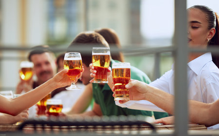 Young people sitting on terrace of urban pub, and clinking their beer mugs, celebrating meeting after long years. Selective focus.の写真素材
