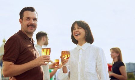 Man and woman enjoy beautiful sunny day, talking and relaxing, drinking beer on sunlit terrace. Festive atmosphere.の写真素材