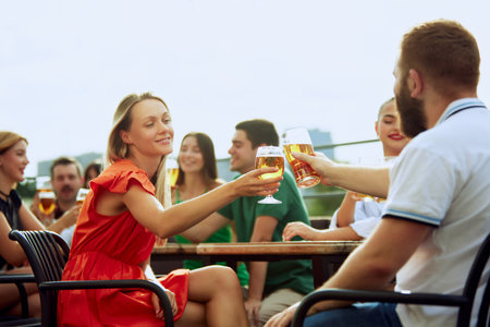 Group of friends sitting at pub terrace talking, drinking alcohol, celebrating meeting after long years. Festive atmosphere.の写真素材