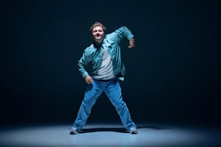 Artistic and joyful young man in casual clothes in motion on stage, performing hip hop against navy blue backgroundの写真素材