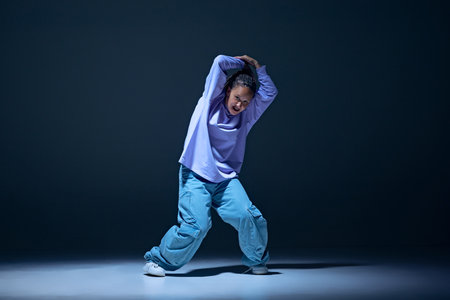 Dynamic image of young girl, passionate dancer in oversized clothes dancing hip hop with energy...