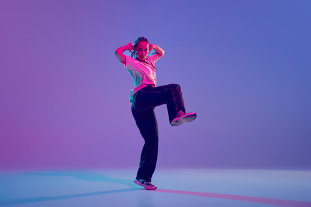 Dance school. Stylish and artistic young girl dancing hip hop with emotions against gradient purple background in neon lightの写真素材