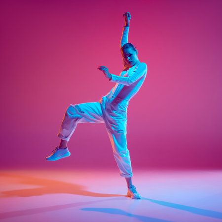 Display of rhythm and style. Young talented girl, dance in motion, training, performing hip-hop against pink background in neon lightの写真素材