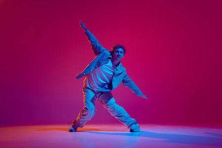 Dance club member. Young energetic man in casual clothes in motion, dance hip hop against pink background in neon lightの写真素材
