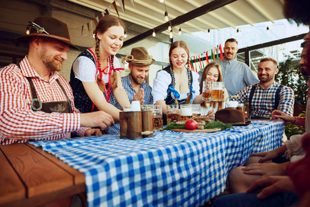 Two women, waitress dressed in Bavarian clothes serving beer to a group of friends meeting at pub for cheerful celebrationの写真素材