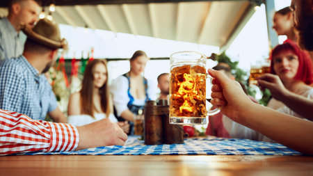 Focus on lager beer mug and blurred people, friends sitting at table at bar and celebrating, drinking, talking