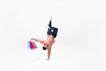 Dynamic image of young man in casual clothes doing one-handed handstand in breakdance pose with...
