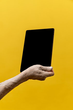 Zombie-like hand holding tablet with blank screen against yellow background. News, sales, announcementの写真素材
