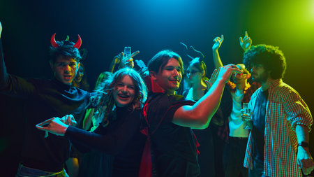 Lively Halloween party scene at nightclub with young people,be friends in costumes and makeup, celebrating holiday with fun and joy, laughing and dancing.の写真素材