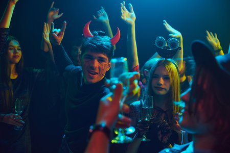 Group of young friends, dressed in spooky and fun costumes, attending nightclub for cheerful celebration of Halloweenの写真素材