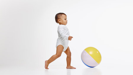 Little baby, girl in onesie walking confidently towards colorful ball, playing with curiosity and...