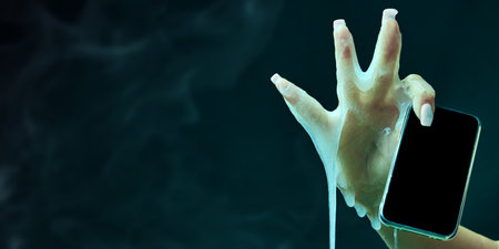 Female hand covered in slime, holding mobile phone against cyan green background. Social media, news, online servicesの写真素材