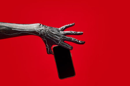 Skeleton hand holding mobile phone with blank screen against red background. Digital marketing promotion, social media post, newsの写真素材