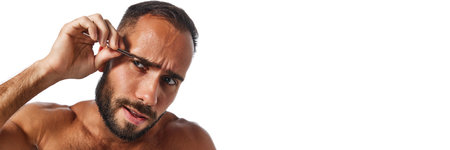 Portrait of handsome young bearded man taking care after his appearance, using tweezers, plucking eyebrows isolated on white studio backgroundの写真素材
