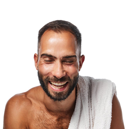 Young shirtless smiling man doing morning routine, washing face, taking care after appearance isolated on white studio backgroundの写真素材