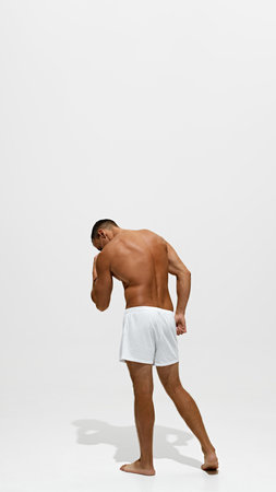 Full-length back view image of muscular shirtless man posing in underwear isolated on white studio background. Strong backの写真素材