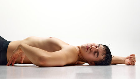Handsome young guy posing shirtless in underwear, lying on floor in relaxed pose isolated on white studio backgroundの写真素材