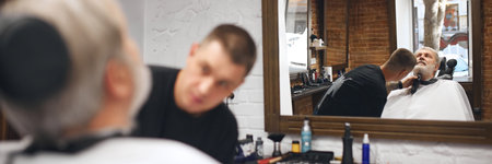 Focused man, barber trimming underside of the client chin with electric trimmer. Senior man visiting barbershopの写真素材