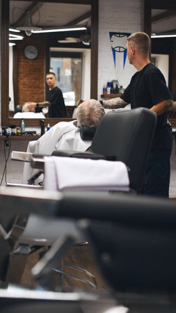 Barber leaning over reclined client, carefully trimming his beard. Client appears comfortable and relaxed in reclining chairの写真素材