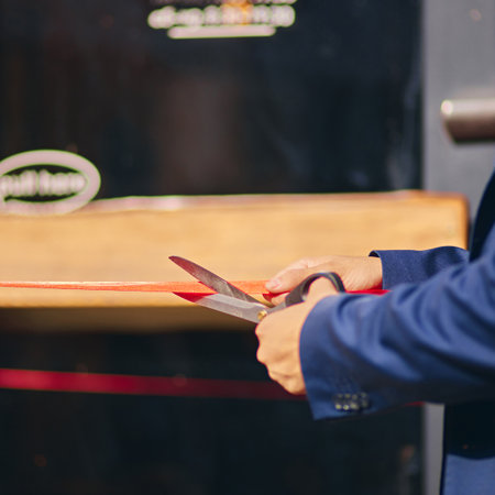 Close-up. Businessman, owner cutting red ribbon, symbolizing official launch and opening of new business venturesの写真素材