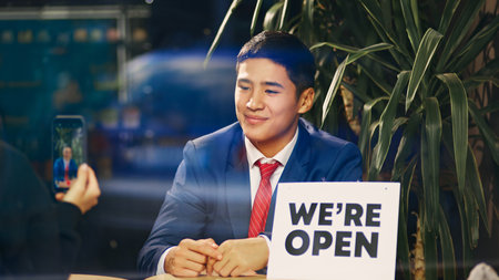 Behind glass winding, someone taking a photo of businessman in blue suit sitting with we are open...