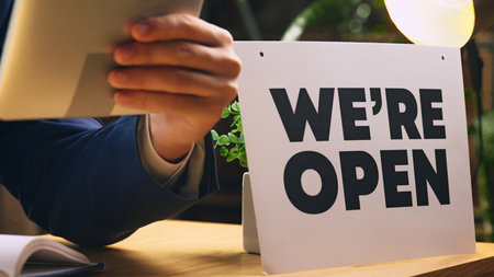 Businessman in formal wear sitting at desk with we are open sign, holding tablet and making notes. Cropped imageの写真素材