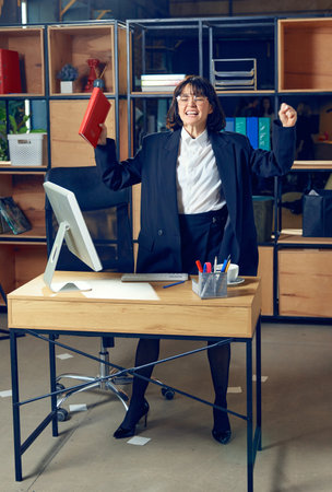 Emotional young woman in formal wear standing in office and expressing pure excitement, symbolizing triumph in her businessの写真素材