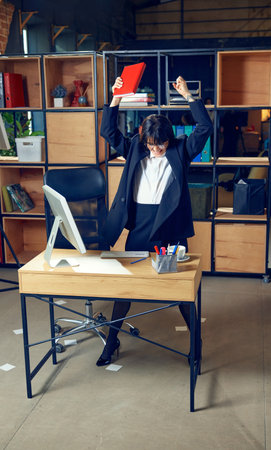 Emotional young woman in formal wear standing in office and expressing pure excitement, symbolizing triumph in her businessの写真素材