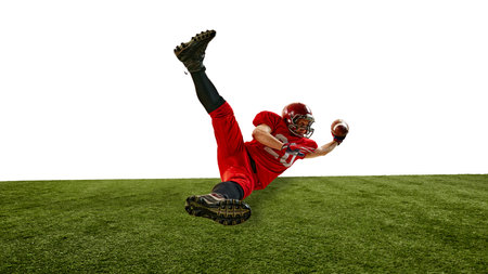 Dynamic image of competitive American football player in red uniform in motion during intense training, falling down on grass while catching the ball.の写真素材