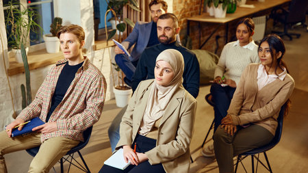 Multiracial group of business people listening attentively during seminar in modern workspace. Corporate learning in dynamic environment.の写真素材