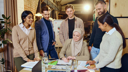 Diverse group of young professionals gathered around table, discussing and working together on...