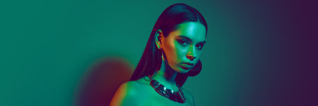 Portrait of young beautiful woman adorned with metallic accessories, set against gradient teal background in neon lightの写真素材