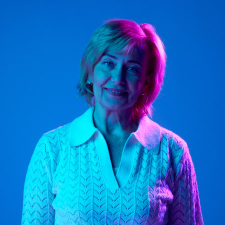 Portrait of smiling, elderly, mature woman in white clothes looking at camera, posing against blue...