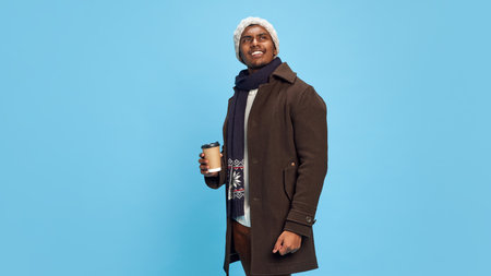 Portrait of happy, young smiling Indian man wearing cozy, warm winter outfit, coat and hat, standing...