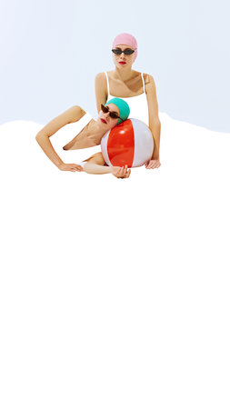 Two women wearing retro swim caps and sunglasses, posing with colorful beach ball on white...