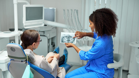Dentist reviews X-ray with mature woman, patient, explaining details and preparing them for next steps in their dental care.の写真素材